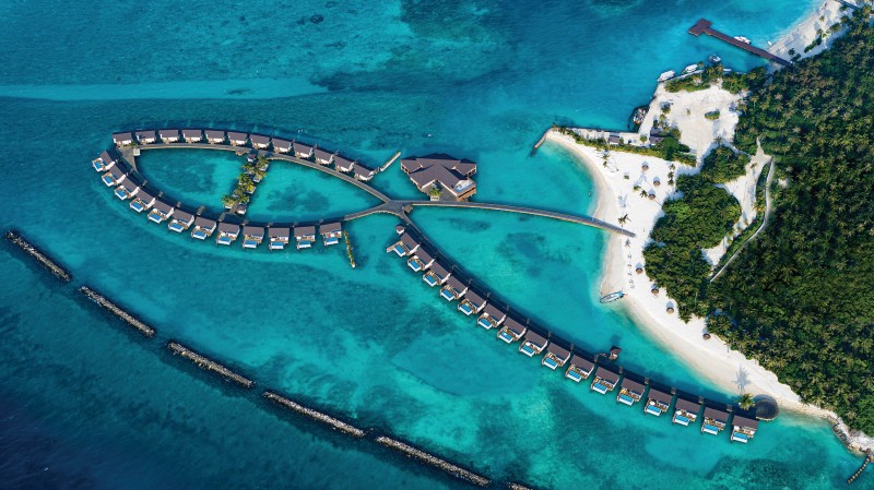 Blick auf die Water Villen und die Resortinsel Luftaufnahme eines luxuriösen Strandresorts mit einem einzigartig gestalteten Pool, der von tropischer Vegetation umgeben ist. Die Anlage zeigt mehrere Chalets mit spitz zulaufenden Dächern, eine hölzerne Sonnenterrasse mit Liegestühlen und eine kleine überdachte Sitzecke. Drei Personen entspannen im und am Pool, umgeben von leuchtend blauem Wasser.