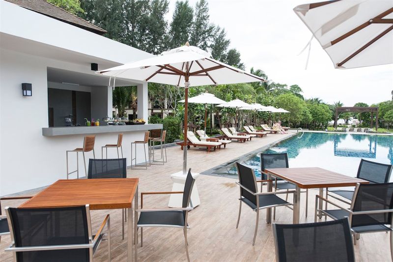 Poolbar im Layana Resort & Spa Außenbereich eines Resorts mit Swimmingpool, Sonnenliegen und einer Poolbar. Es sind Terrassenmöbel unter Sonnenschirmen aufgestellt, und im Hintergrund ist eine üppige Bepflanzung zu erkennen.