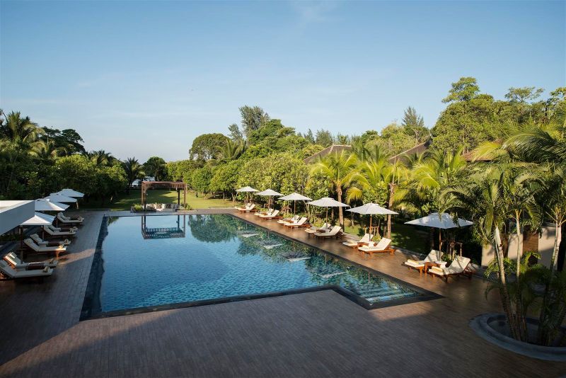 Swimmingpool im Layana Resort & Spa Ein luxuriöses Schwimmbad im Freien umgeben von üppiger Vegetation und Liegestühlen unter weißen Sonnenschirmen bei Tageslicht.