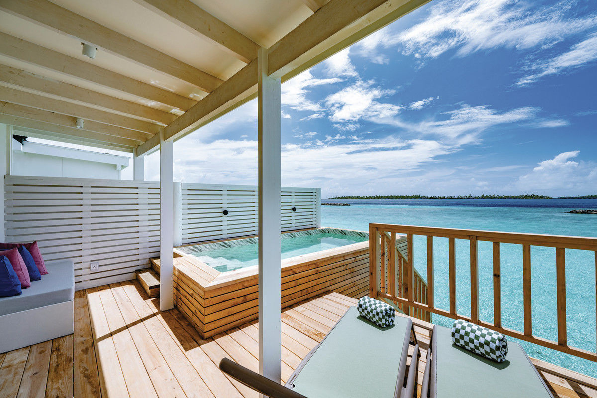Terrasse einer Lagoon Villa mit Pool Eine luxuriöse Terrasse mit Whirlpool und Sitzgelegenheiten, mit Blick auf das türkisfarbene Meer und eine idyllische Inselkulisse unter blauem Himmel.