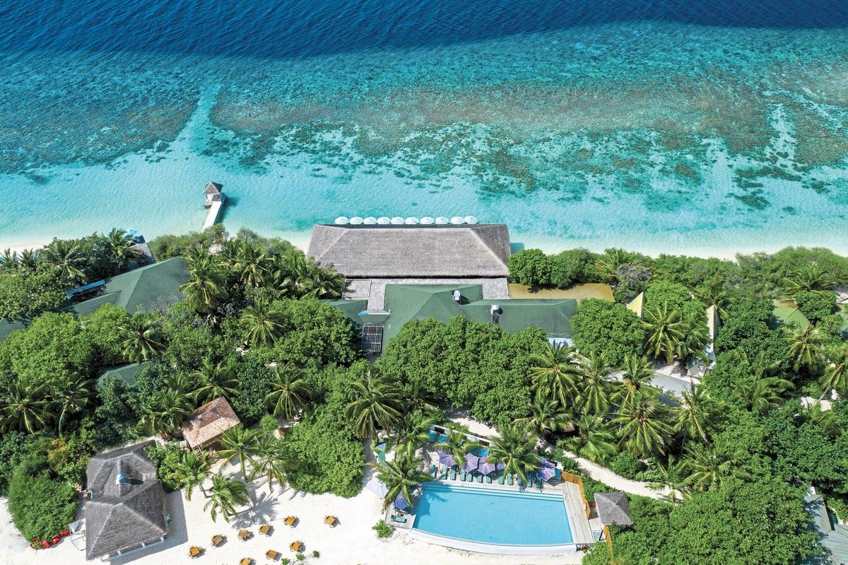 Blick auf das OBLU NATURE Helengeli by Sentido Luftaufnahme eines luxuriösen Inselresorts mit üppiger Vegetation, umgeben von klarem, türkisfarbenem Wasser. Hervorzuheben ist ein großer Swimmingpool neben Strandliegen und ein traditioneller Leuchtturm am Ende eines Stegs.