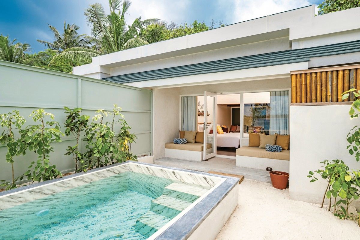Two Bedroom Family Villa mit Pool Ein modernes, stilvolles Strandhaus mit offenen Türen, das auf eine gemütliche Innen-lounge mit Kissen und einem Bett blickt. Im Vordergrund ein kleiner privater Pool umgeben von tropischen Pflanzen. Die Szenerie vermittelt ein Gefühl von Ruhe und Luxus.