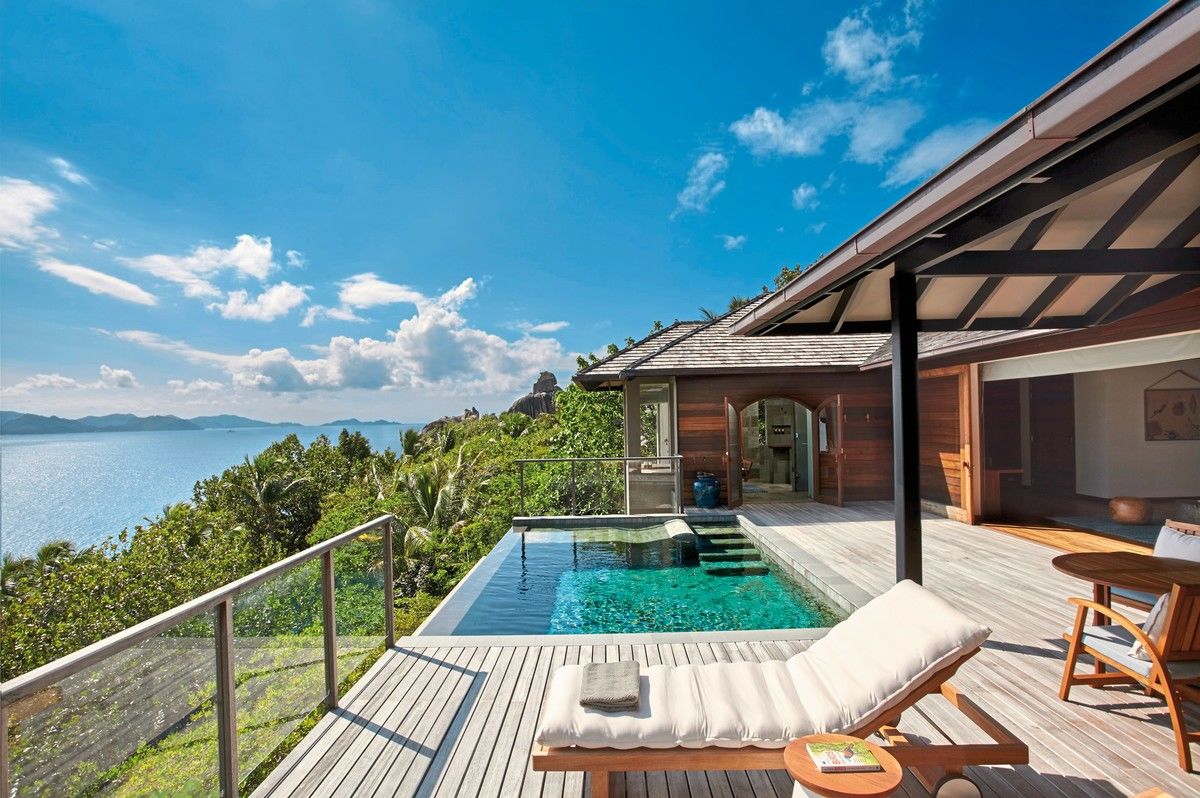 Panorama Pool Villa Ein luxuriöses Ferienhaus mit Holzveranda, privatem Pool und atemberaubender Aussicht auf das Meer und eine tropische Inselkette. Der Himmel ist klar und blau mit einigen weißen Wolken.