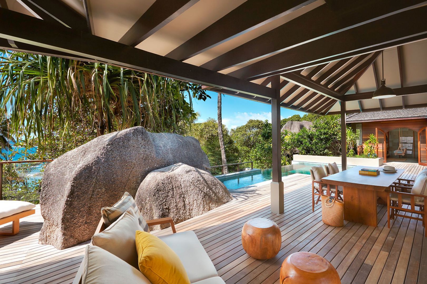 Two Bedroom Pool Villa Luxuriöse Außenterrasse mit Holzboden und modernen Gartenmöbeln, integriertem Swimmingpool und einem beeindruckenden Felsblock, umgeben von tropischer Vegetation unter einem blauen Himmel.