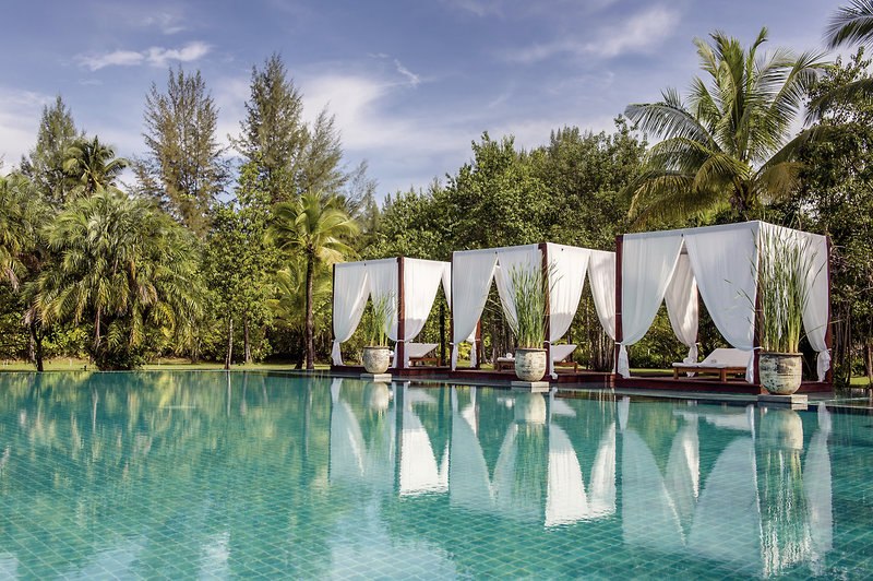 Pool Ein luxuriöses Swimmingpool-Resort umgeben von üppigem tropischem Grün. Vier elegante, weiße Cabanas mit Vorhängen stehen am Rand des hellblauen Pools, reflektieren sich im ruhigen Wasser und bieten ein Bild von Entspannung und Ruhe.