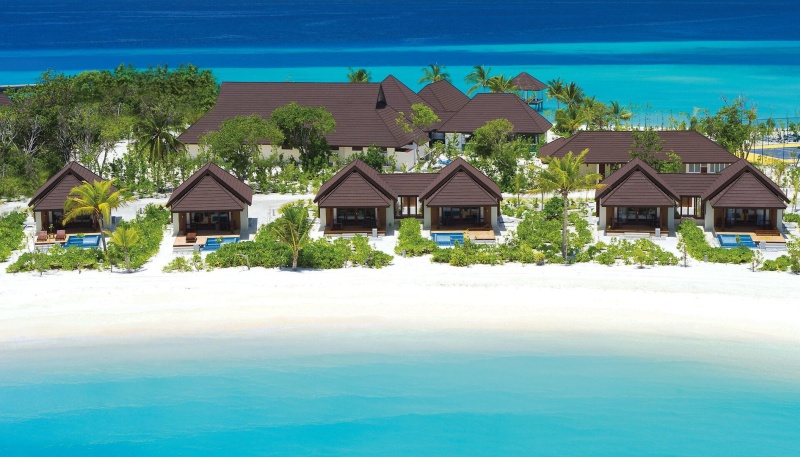 Beach Villen Luxuriöser Strandresort mit Reihen von Holzbungalows, flankiert von üppigem Grün und weißem Sandstrand, gelegen an einem klaren türkisfarbenen Meer.