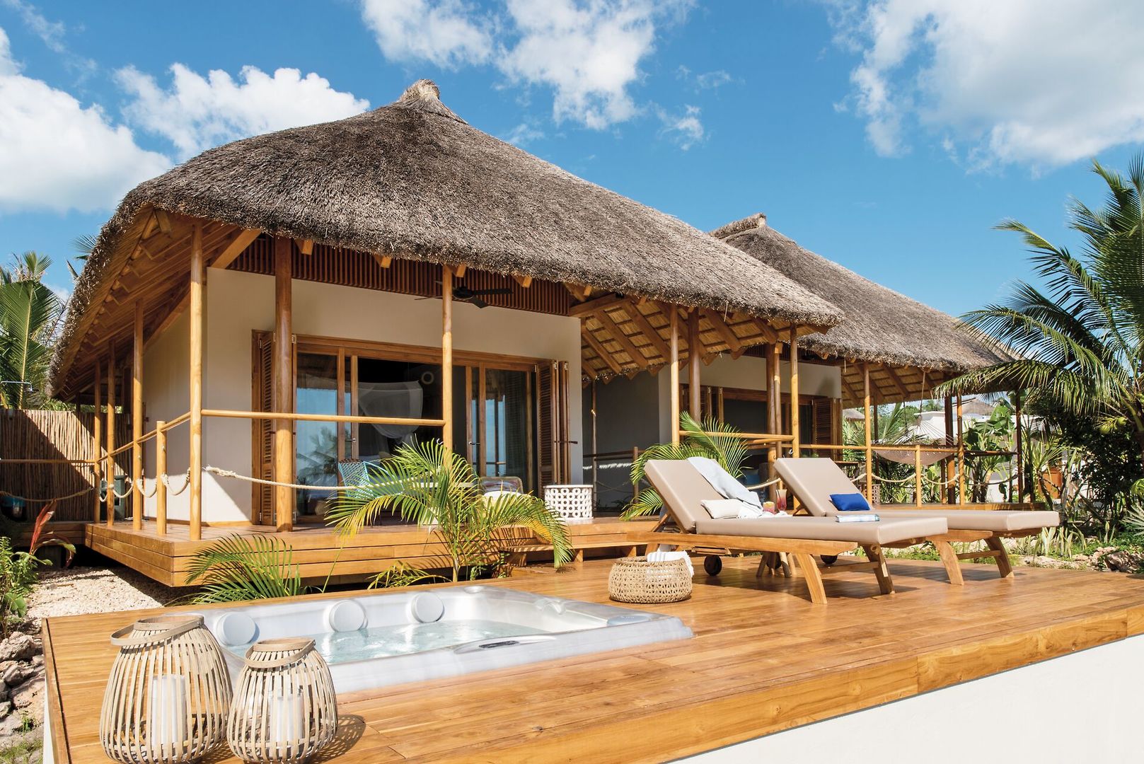Ocean Front Suite Luxuriöses Strandhaus mit Strohdach, Terrasse und Whirlpool, umgeben von tropischer Vegetation unter klarem blauem Himmel.