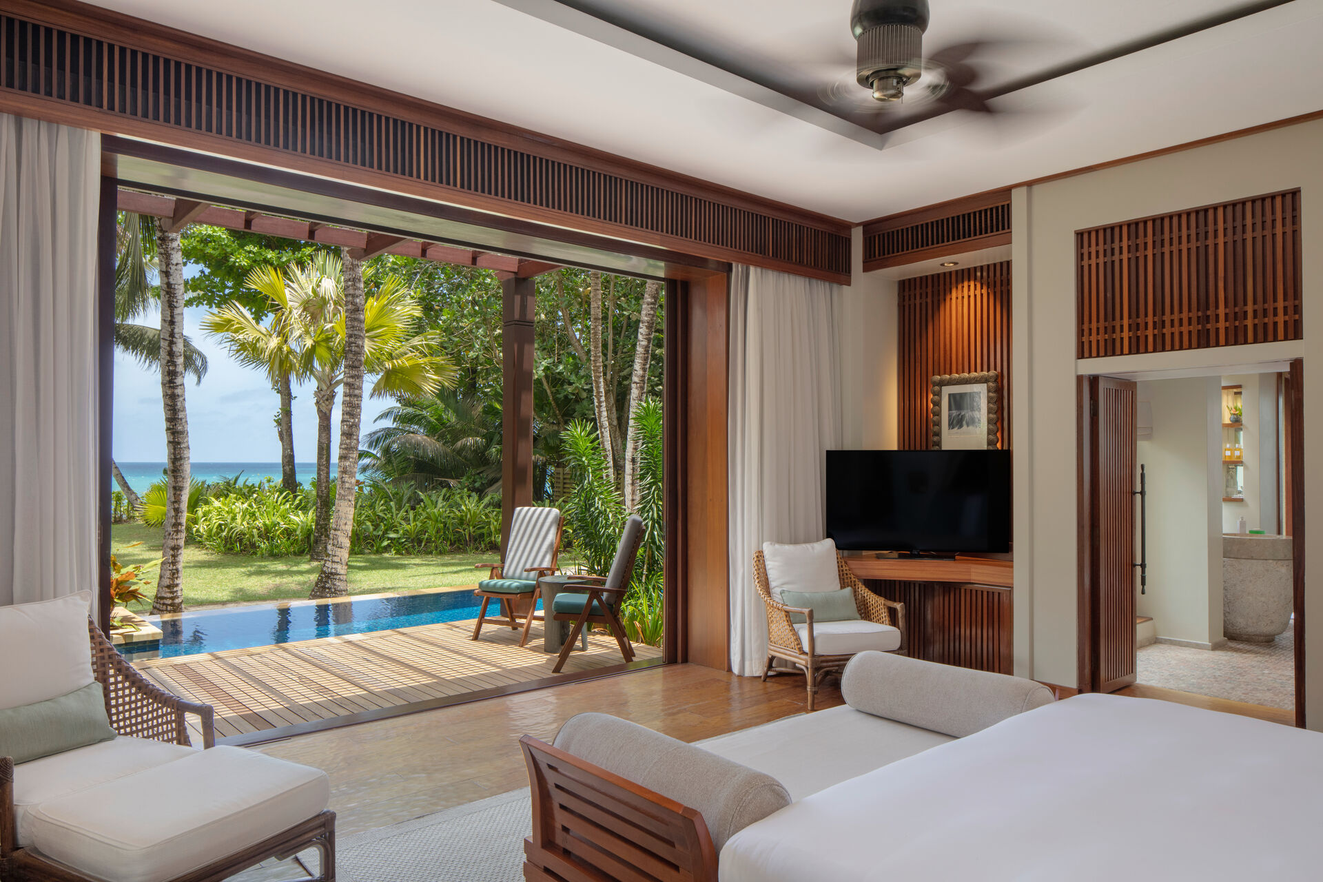 Zimmerbeispiel Luxuriöse Hotelzimmer mit elegantem Design, das ein nahtloses Innen-Außen-Wohngefühl mit offenem Zugang zu einer Terrasse mit privatem Pool und tropischer Gartenlandschaft bietet. Im Zimmer moderne Möbel, ein großes Bett und ein Flachbildfernseher.