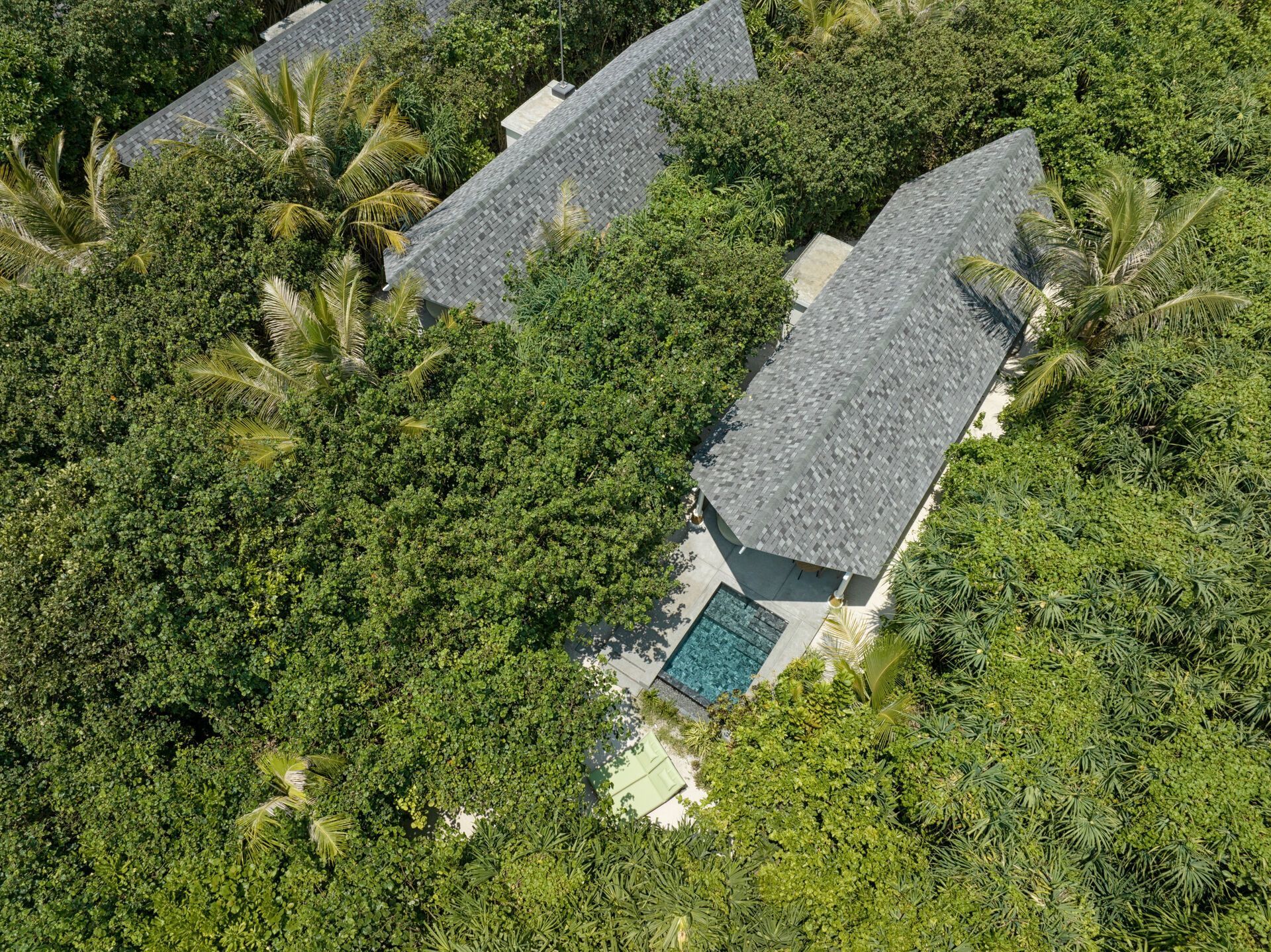 Luftaufnahme eines luxuriösen Resorts versteckt im dichten tropischen Grün mit Schieferdächern und einem sichtbaren Swimmingpool.