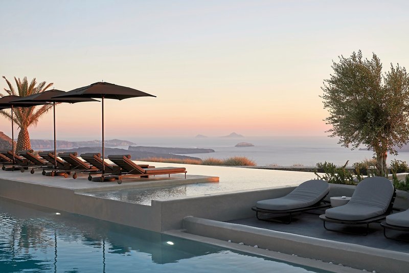 Aussicht Bild eines luxuriösen Infinity-Pools bei Sonnenuntergang mit Liegestühlen und Sonnenschirmen mit Blick auf das ruhige Meer und Inseln am Horizont.
