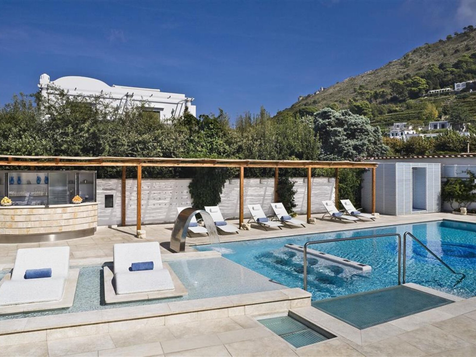 Poolbereich Außenansicht eines luxuriösen Poolbereichs mit Sonnenliegen und Blick auf einen grünen Hügel.