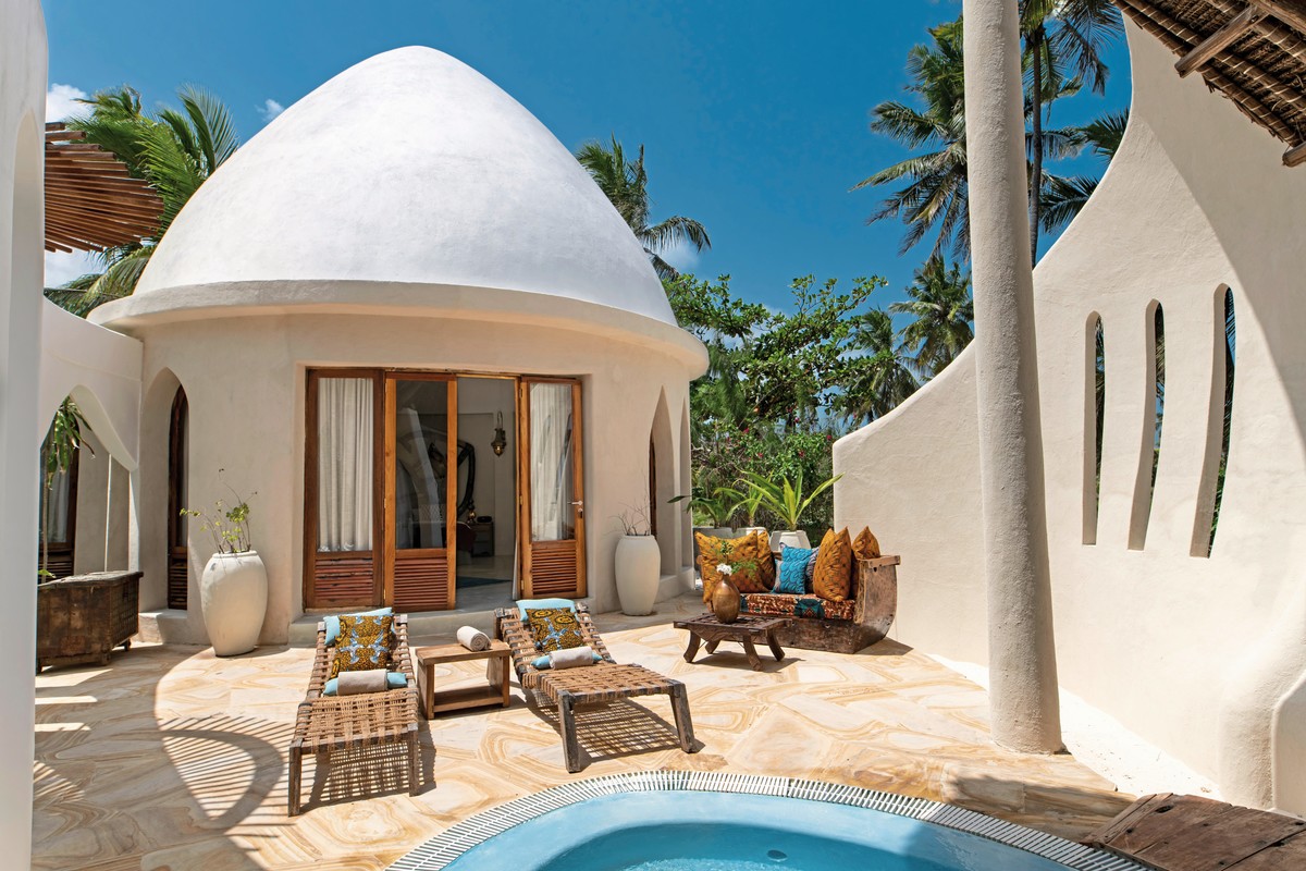 Ein luxuriöses, kuppelförmiges Strandhaus mit großen Fenstern und Holztüren. Vor dem Haus befinden sich eine Terrasse mit zwei Liegestühlen und ein kleiner Pool. Umgeben ist das Anwesen von tropischer Vegetation und Palmen, was eine ruhige und entspannende Atmosphäre kreiert.