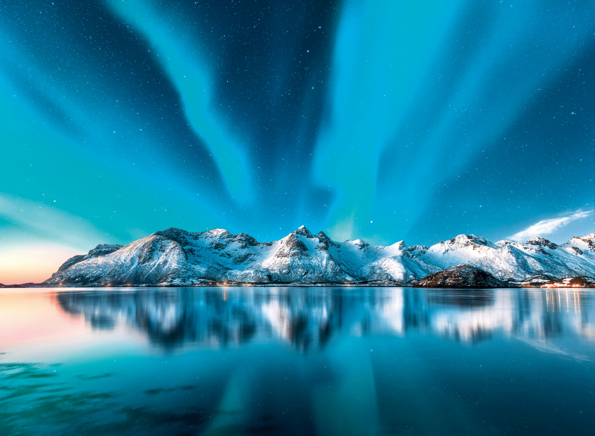 Polarlichter Ein strahlendes Nordlicht über einer verschneiten Gebirgslandschaft mit Spiegelung im klaren See bei Nacht.